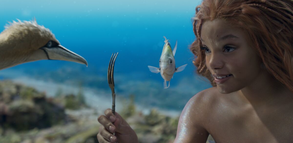 Halle Bailey as Ariel holds up a fork as Flounder and Scuttle look on.