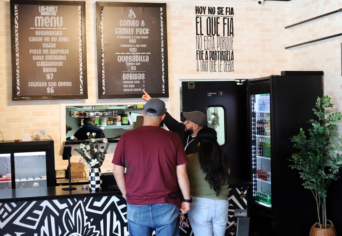 Omar De la Vega, co-owner of Los Juarez Burritos, helps a customer choose from a menu of burritos.