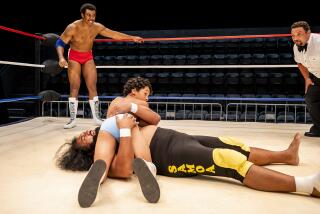 In a  pro wrestling ring a wrestler pretends to be pinned by a young boy as another wrestler looks on.