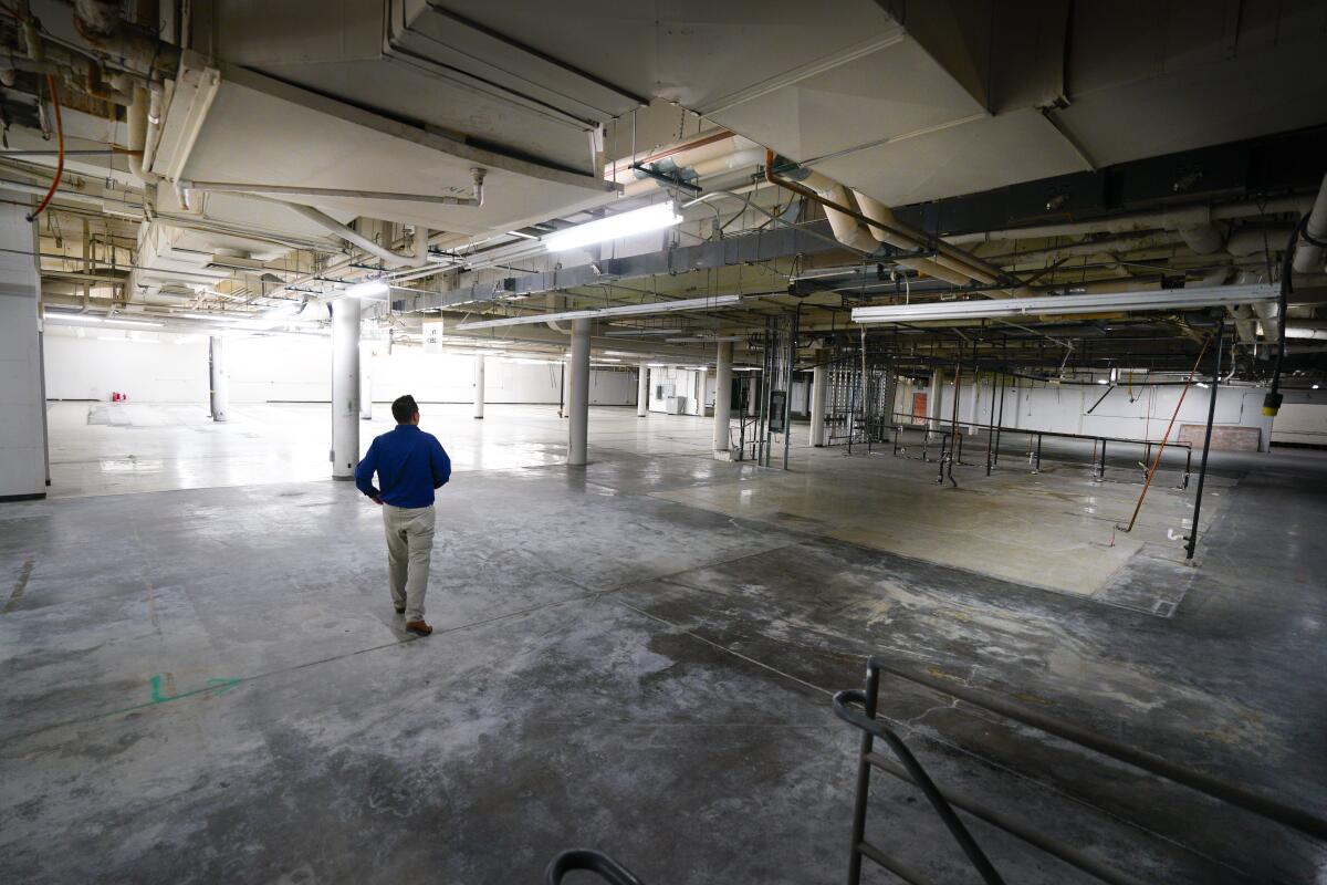 A man stands in an enormous sunlit empty space in a vacant warehouse.