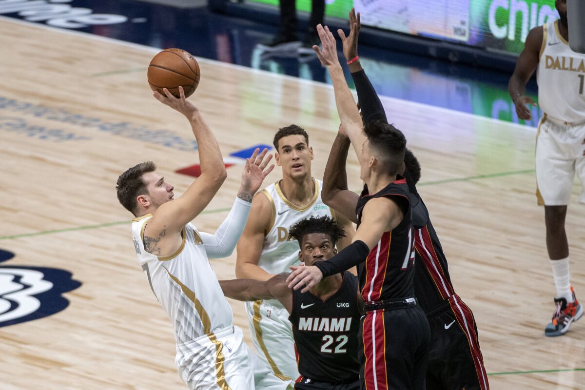 Dallas Mavericks guard Luka Doncic, left, shoots over Miami Heat's Tyler Herro (14) and Bam Adebayo, obscured, as Miami's Jimmy Butler (22) and Dallas' Dwight Powell watch during the first half of an NBA basketball game Friday, Jan. 1, 2021, in Dallas. (AP Photo/Jeffrey McWhorter)
