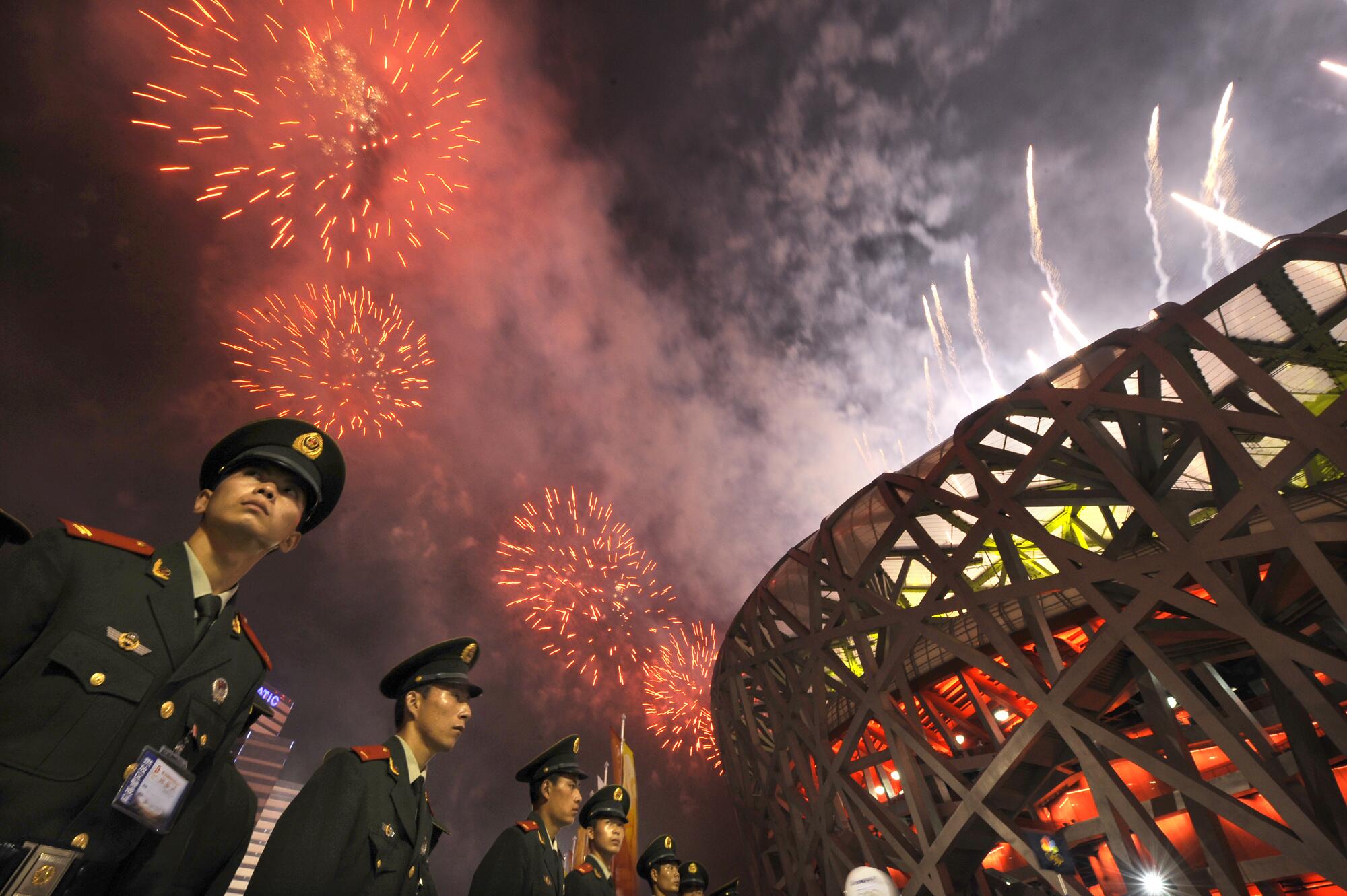 Soldiers stand outside the "Bird's Nest" stadium as fireworks go off above