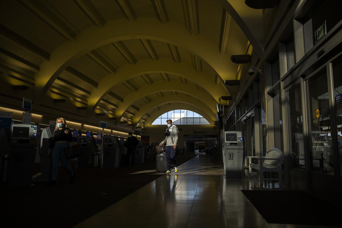 Travelers wear masks as they make their way through John Wayne Airport in Santa Ana on Monday.