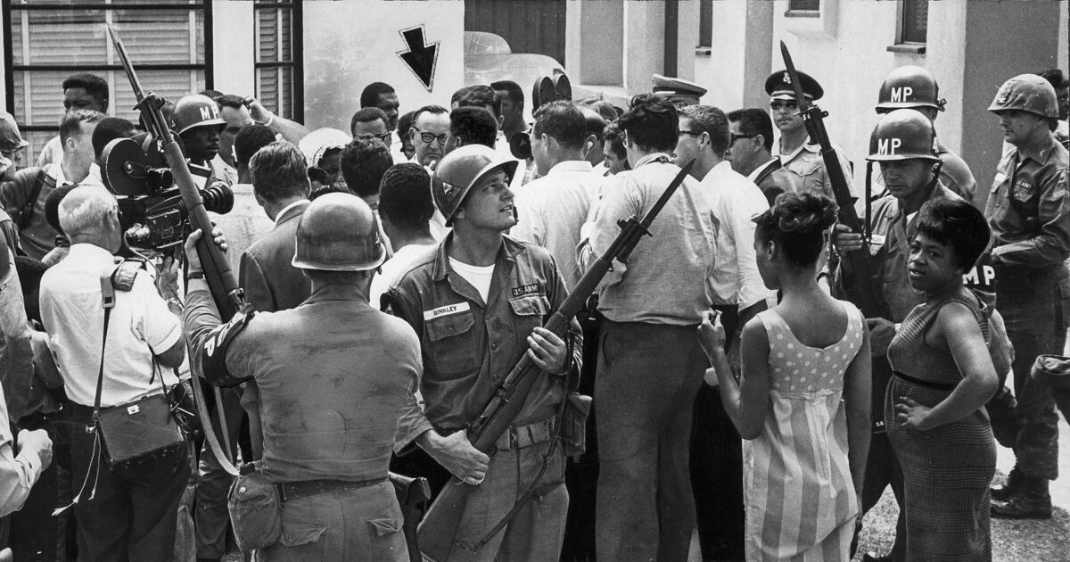 Armed Army soldiers survey a crowd as Governor Pat Brown visits Los Angeles during the 1965 Watts riots