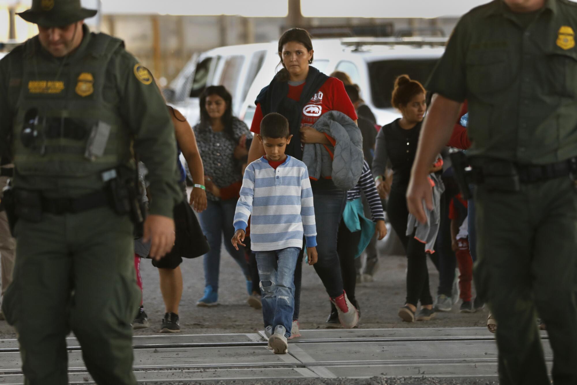 A group of about 50 men, women and children are led by U.S. Border Patrol agents to a holding area in El Paso