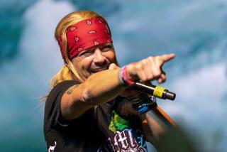 A man wearing a bandana holds a microphone and points his finger 