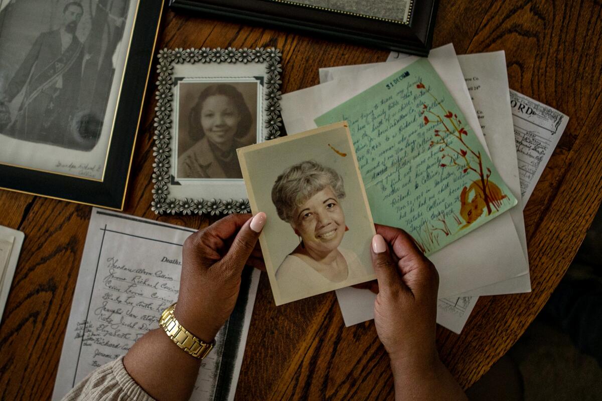 Denise Diggs holds a photo of her late mother as she looks at a table full of old family documents and pictures 