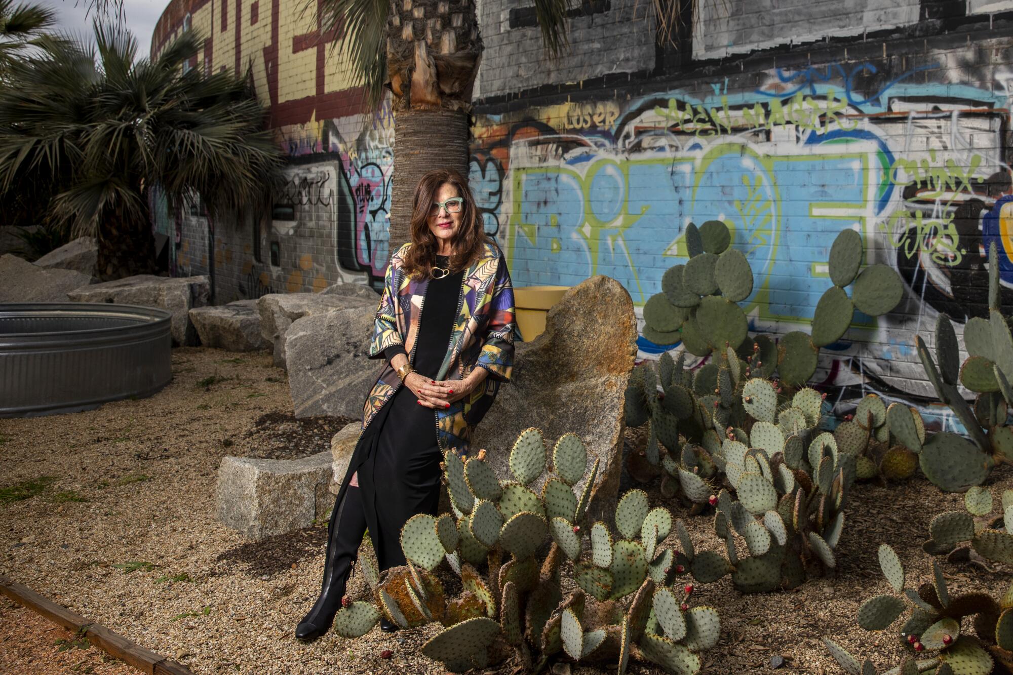 Landscape architect Mia Lehrer sits on a rock in an urban garden planted with cactuses and palms.