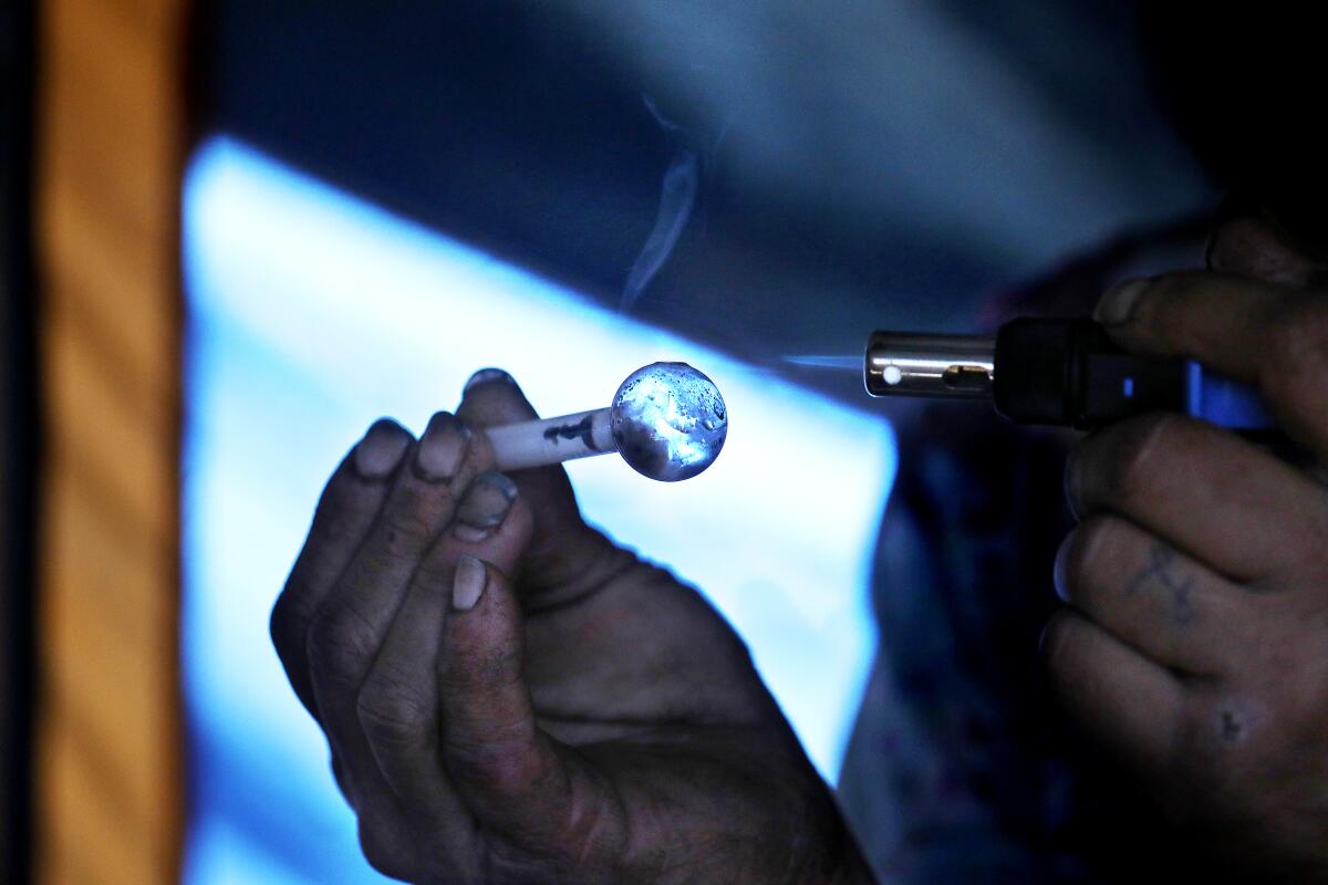 A close-up of hands holding a meth pipe and a lighter 