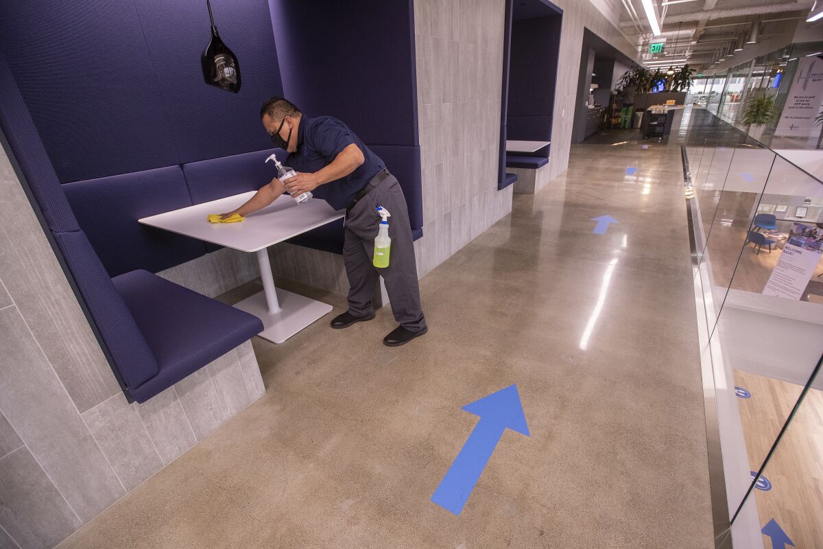 A worker wipes down an office table next to blue arrows on the floor