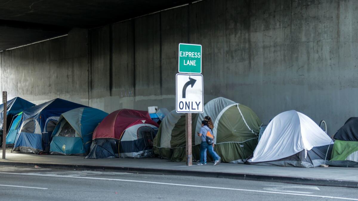 Pedestrians walk past a homeless encampment along 39th Street underneath the 110 Freeway.