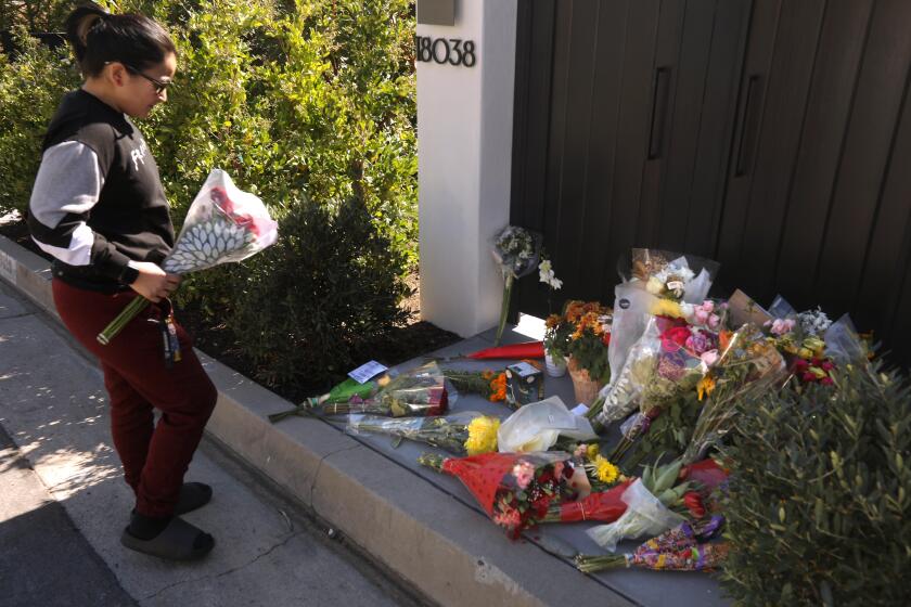 PACIFIC PALISADES, CA - OCTOBER 30, 2023 - Daisy Muro, from Downey, prepares to leave flowers at a growing memorial for actor Matthew Perry in front of his home in Pacific Palisades on October 30, 2023. "It breaks my heart," Muro said about the passing of the Friends television star. "It won't be the same anymore watching, Friends." It's going to be sad because he's not here anymore," Muro concluded. (Genaro Molina / Los Angeles Times)