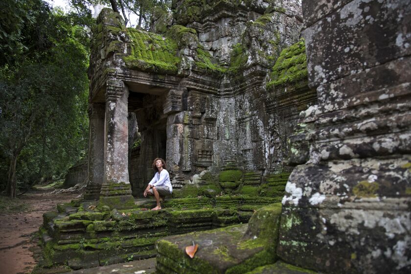 Cambodia - Young traveller, with curly hair, wearing a white long sleeve shirt and light shorts, visiting the ruins of Preah Khan in Angkor Wat
