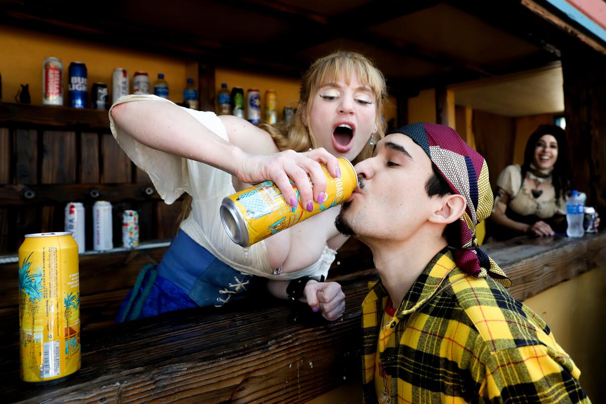 A woman helps a man chug a beer.