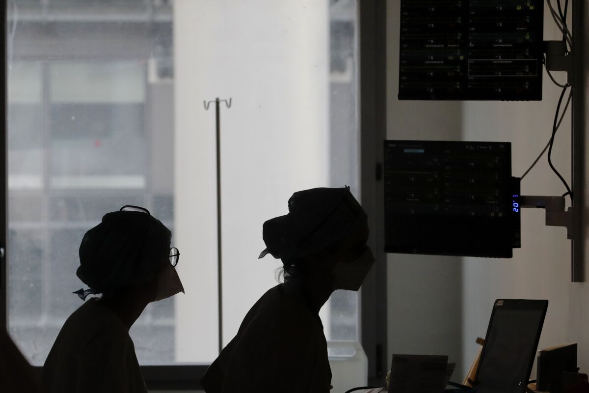 Nurses seen in silhouette track COVID patients on monitors in a hospital ward.