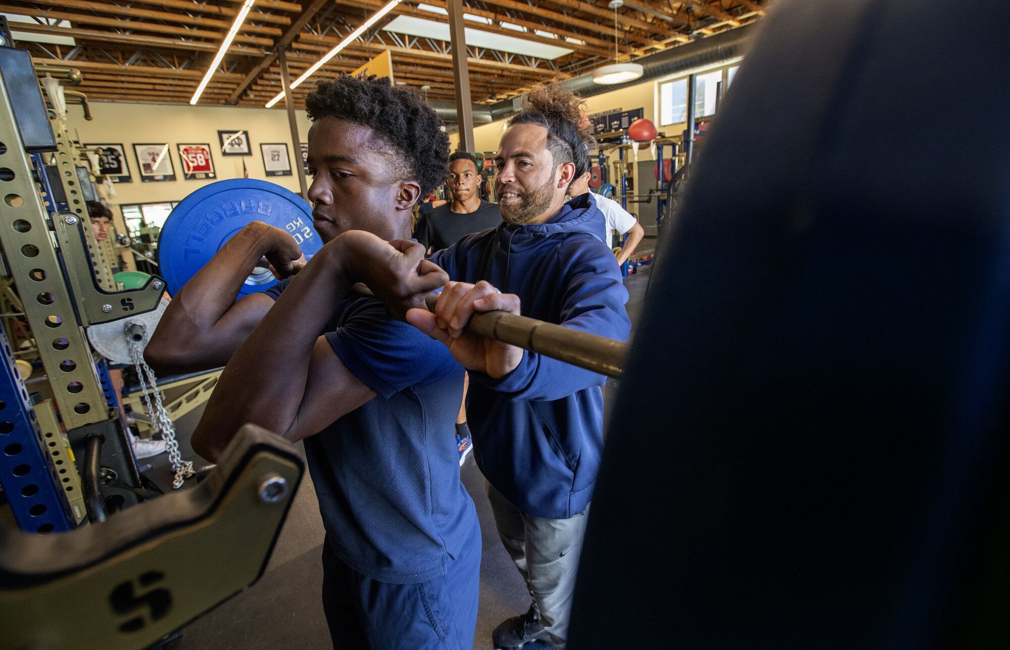 New Notre Dame football coach Evan Yabu helps Amare Johnson, 15, with a front squat exercise during a training session.