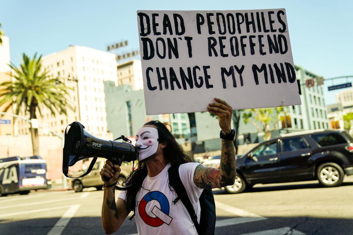 A man in a mask stands on a street with a bullhorn and a sign that says, "Dead pedophiles don't reoffend. Change my mind."