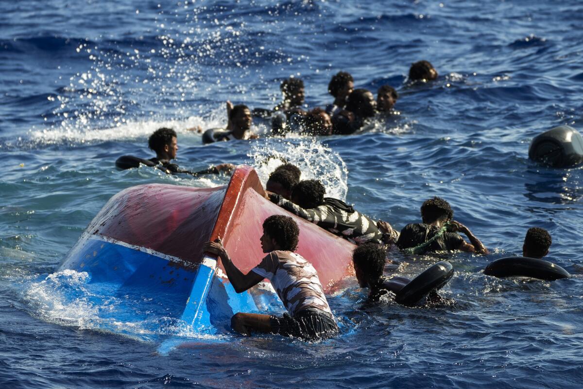 FILE - Migrants swim next to their overturned wooden boat during a rescue operation by Spanish NGO Open Arms at south of the Italian Lampedusa island at the Mediterranean sea, Aug. 11, 2022. The back-to-back shipwrecks of migrant boats off Greece that left at least 22 people dead this week has once again put the spotlight on the dangers of the Mediterranean migration route to Europe. (AP Photo/Francisco Seco, file)