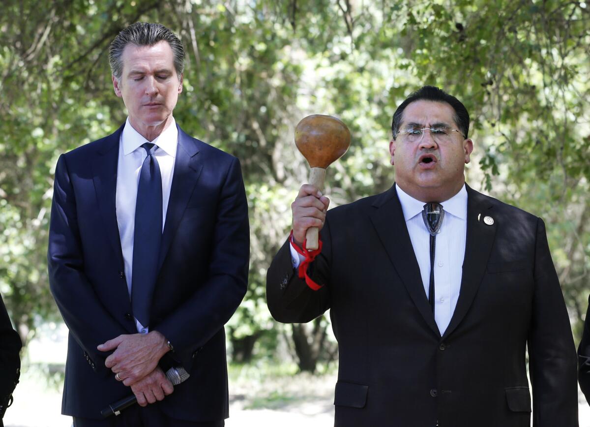Gov. Gavin Newsom, left, bows his head as Assemblyman James Ramos (D-Highland) of the San Manuel Band of Mission Indians opens a meeting Tuesday with tribal leaders from around the state at the future site of the California Indian Heritage Center in West Sacramento.