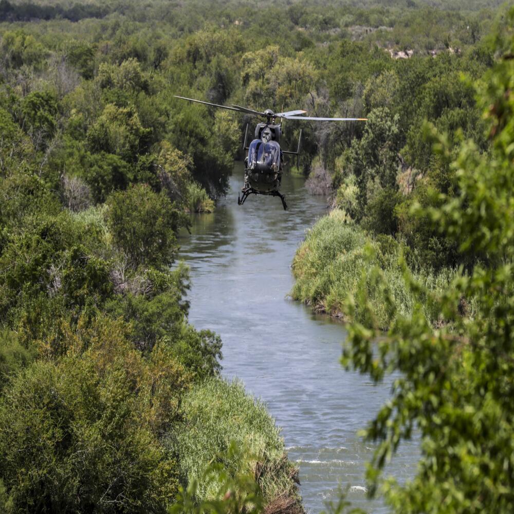 A helicopter flies over a river running through a wooded landscape