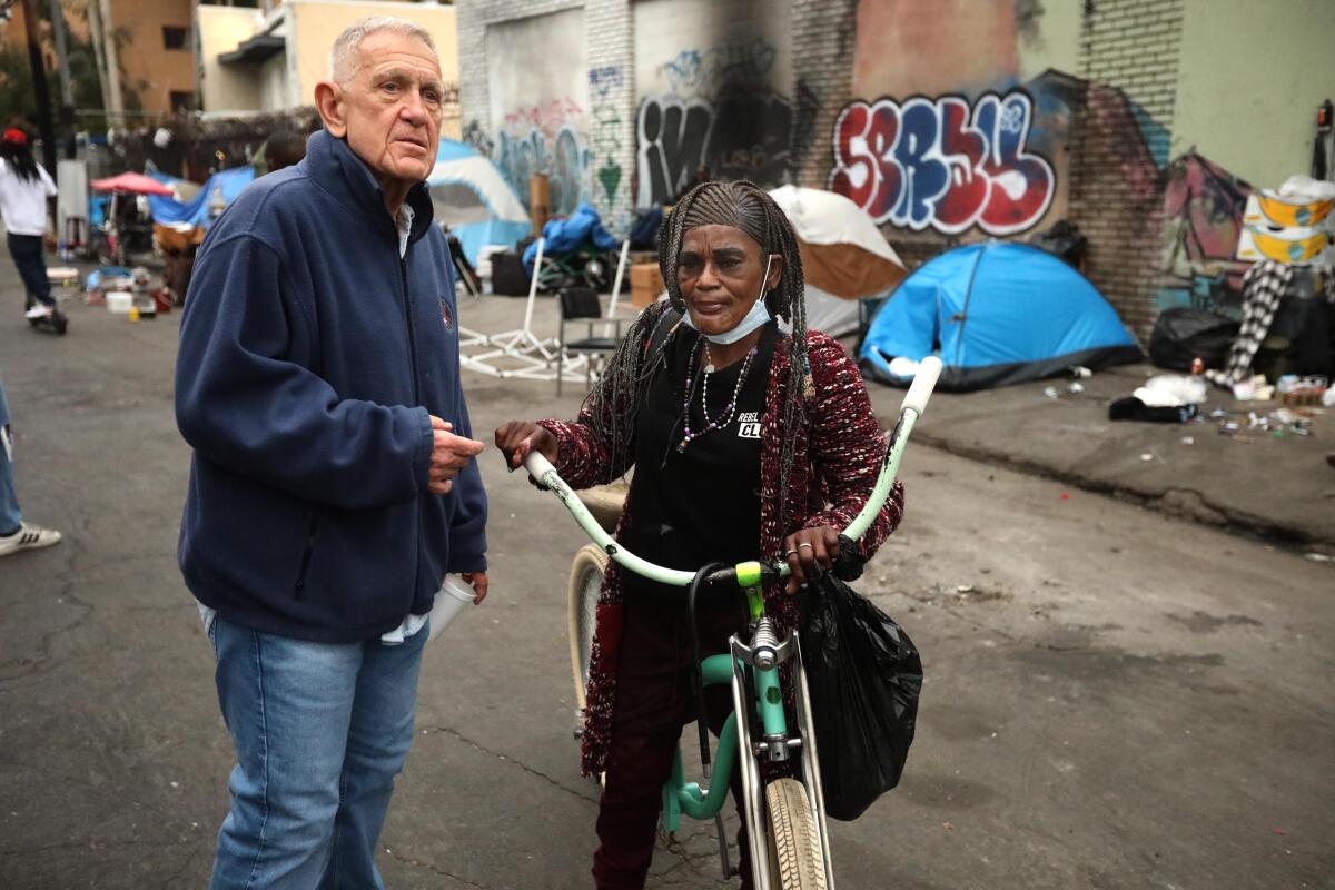 A man speaks with a homeless woman on a bicycle in Skid Row.