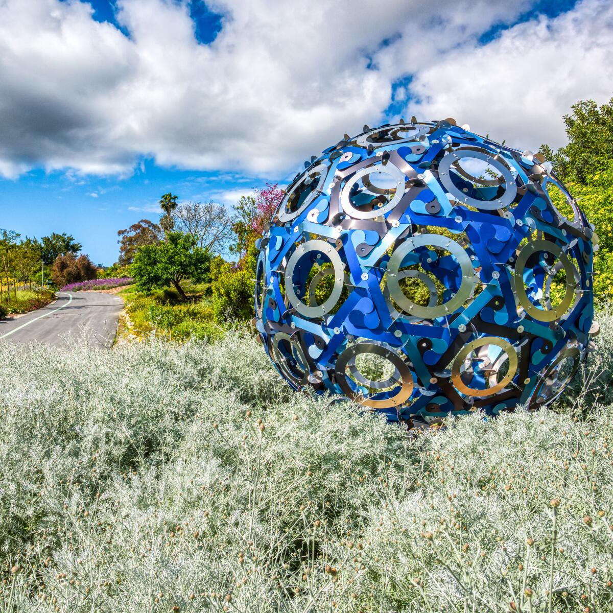 A spherical metal sculpture by Doris Sung, surrounded by plants.