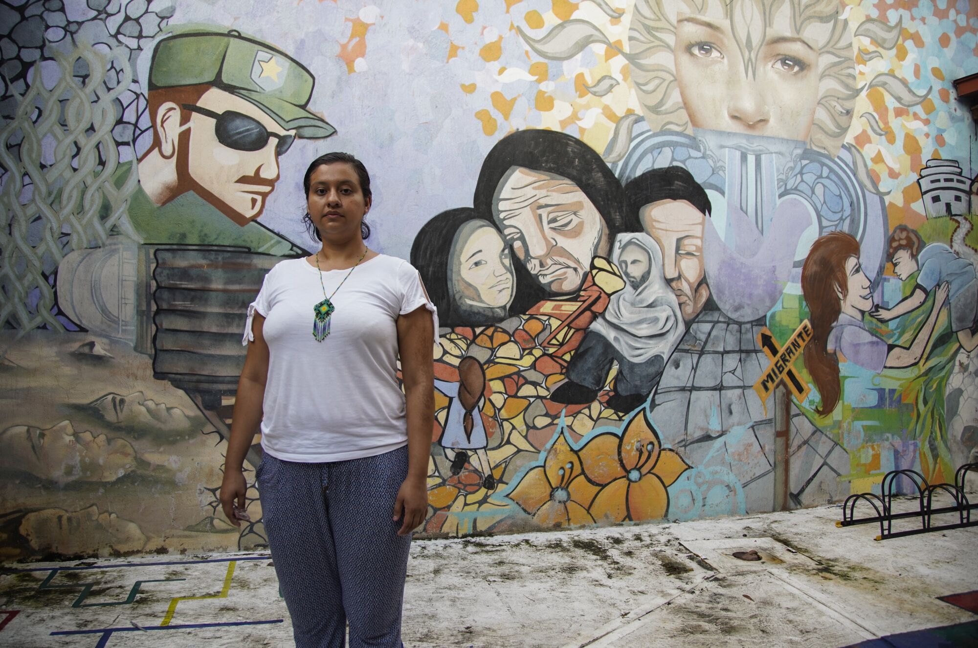 Yuriria Salvador stands in a courtyard in front of a mural of men, women and children