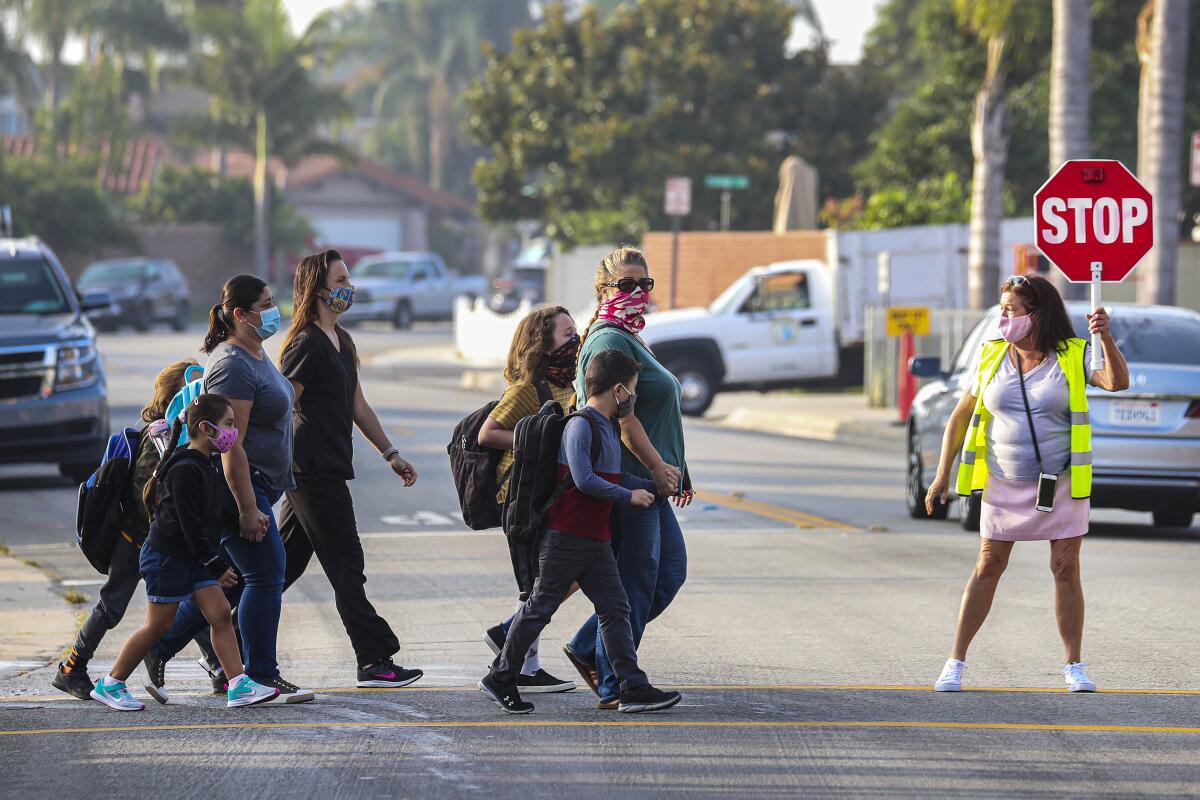 A crossing guard holds a stop sign as parents and young students use the street