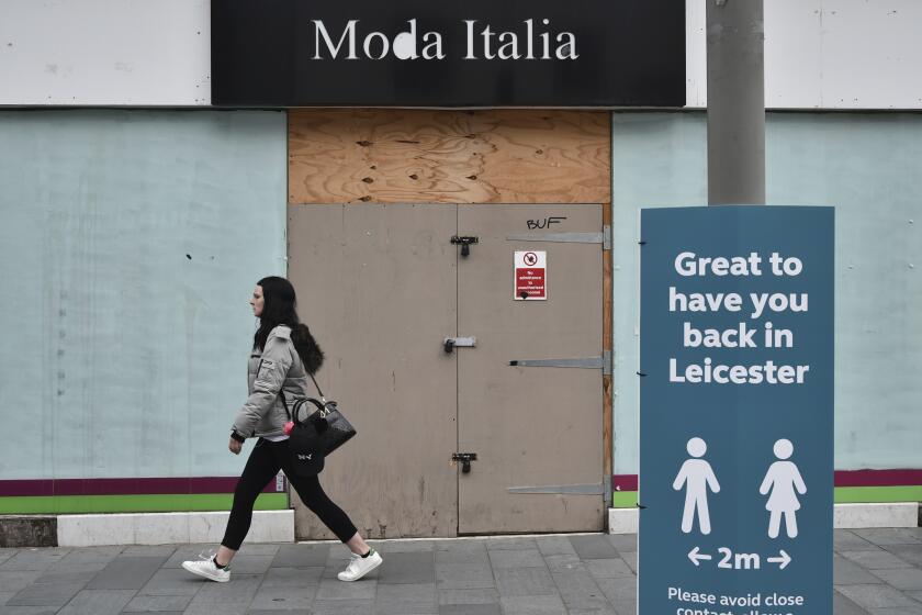 A woman walks past a boarded up shop in Leicester city centre, England, Tuesday June 30, 2020. The British government has reimposed lockdown restrictions in the English city of Leicester after a spike in coronavirus infections, including the closure of shops that don't sell essential goods and schools. (AP Photo/Rui Vieira)