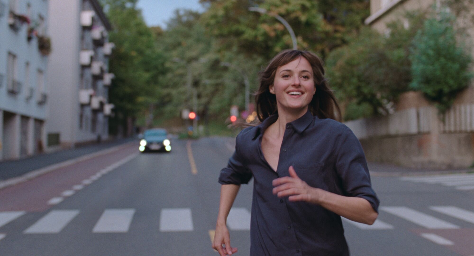 A smiling woman runs down the middle of a street.