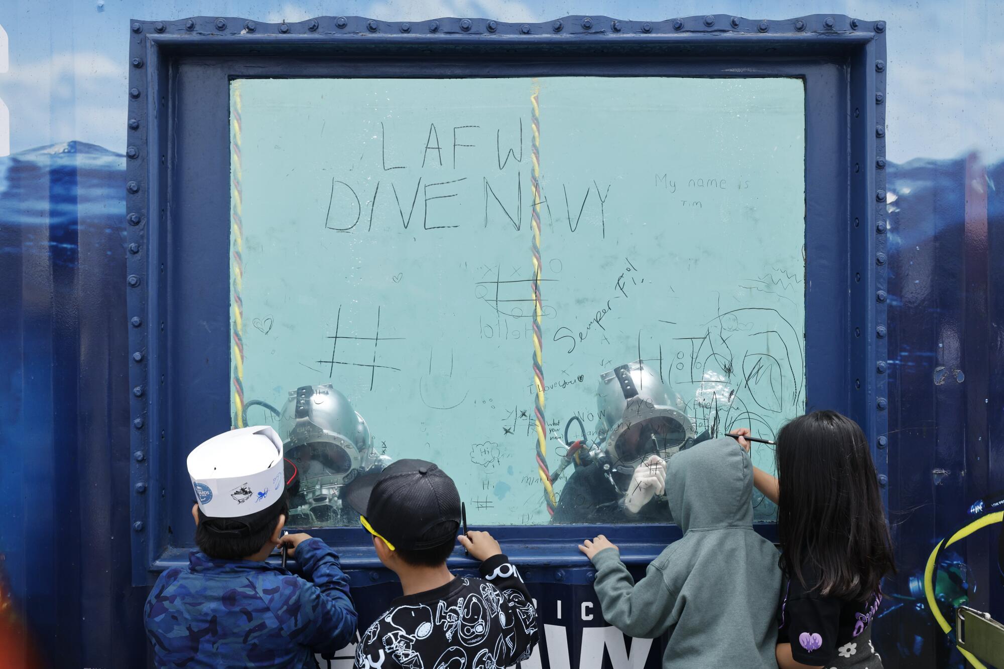 Children watch as Navy divers write with their fingers on glass.