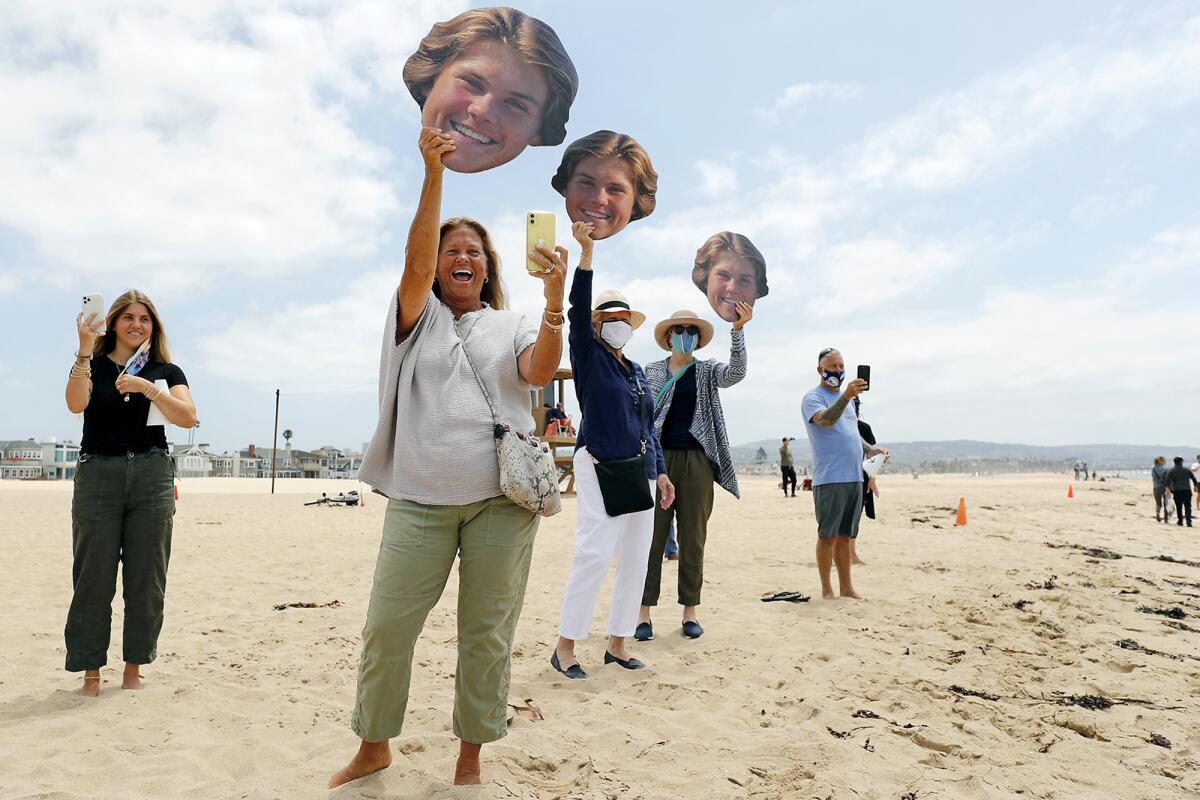 Christy Brigandi cheers and waves a photo of her son Johnny, a Newport Harbor senior, as he joins a graduation walk.