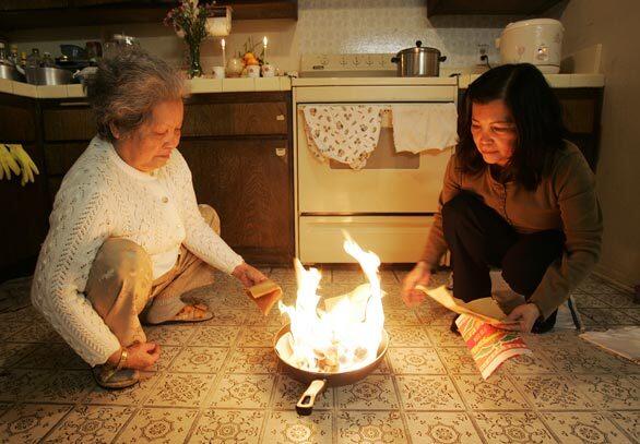 In her Westminster home, Tuyet Tran, left, burns ceremonial paper with her daughter, Trinh Tuyet Tran, in a ritual to benefit kitchen god Ong Tao the week before Tet parties begin. The Year of the Mouse begins Thursday.