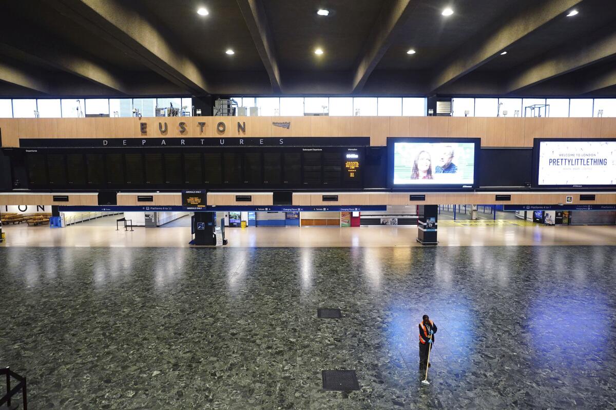 A person sweeps the floor in front of an empty departures board at Euston station, as members of the drivers' union Aslef and the Transport Salaried Staffs Association (TSSA) go on strike, in London, Wednesday, Oct. 5, 2022. (Victoria Jones/PA via AP)