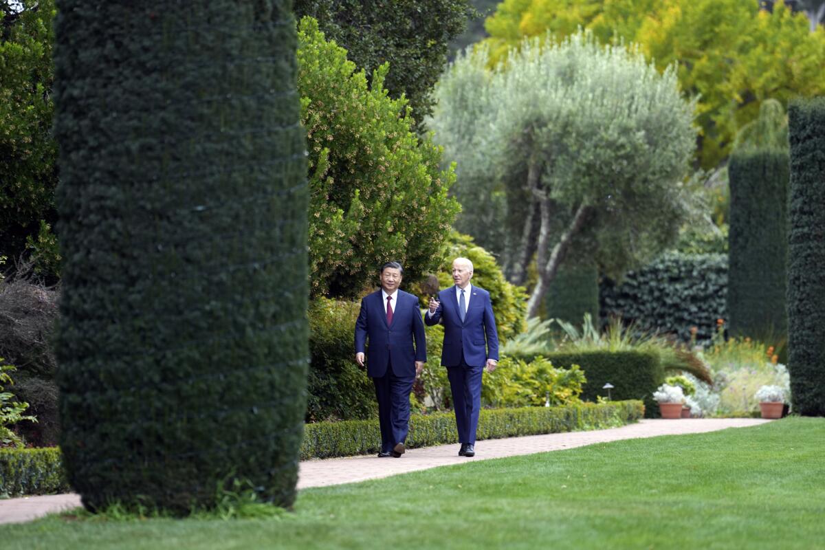 two men in suits walk among a lush garden