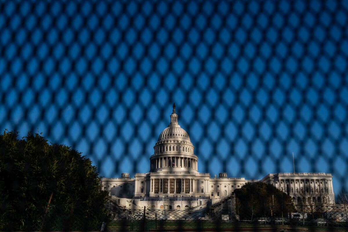 The U.S. Capitol building is seen through a security fence with a blue sky behind it.