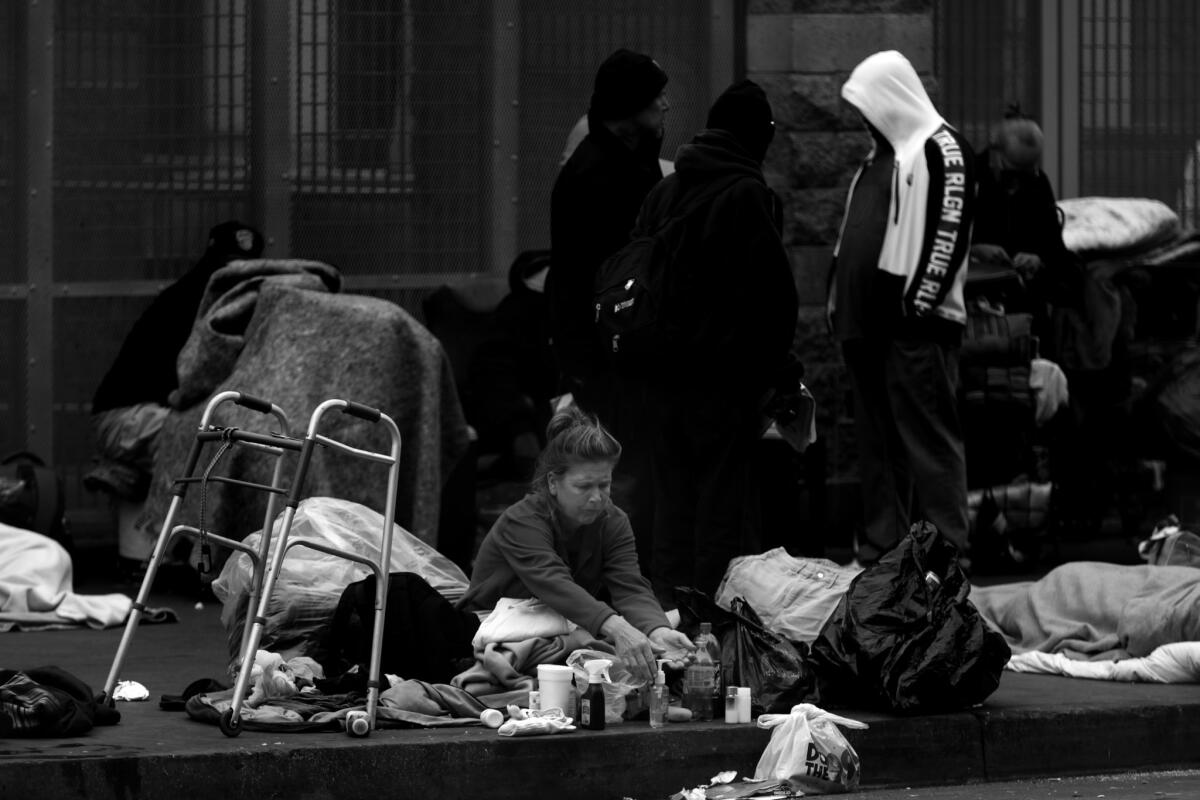 A woman sitting on the sidewalk washes her hands using sanitizer outside the Midnight Mission in the skid row neighborhood of downtown L.A.