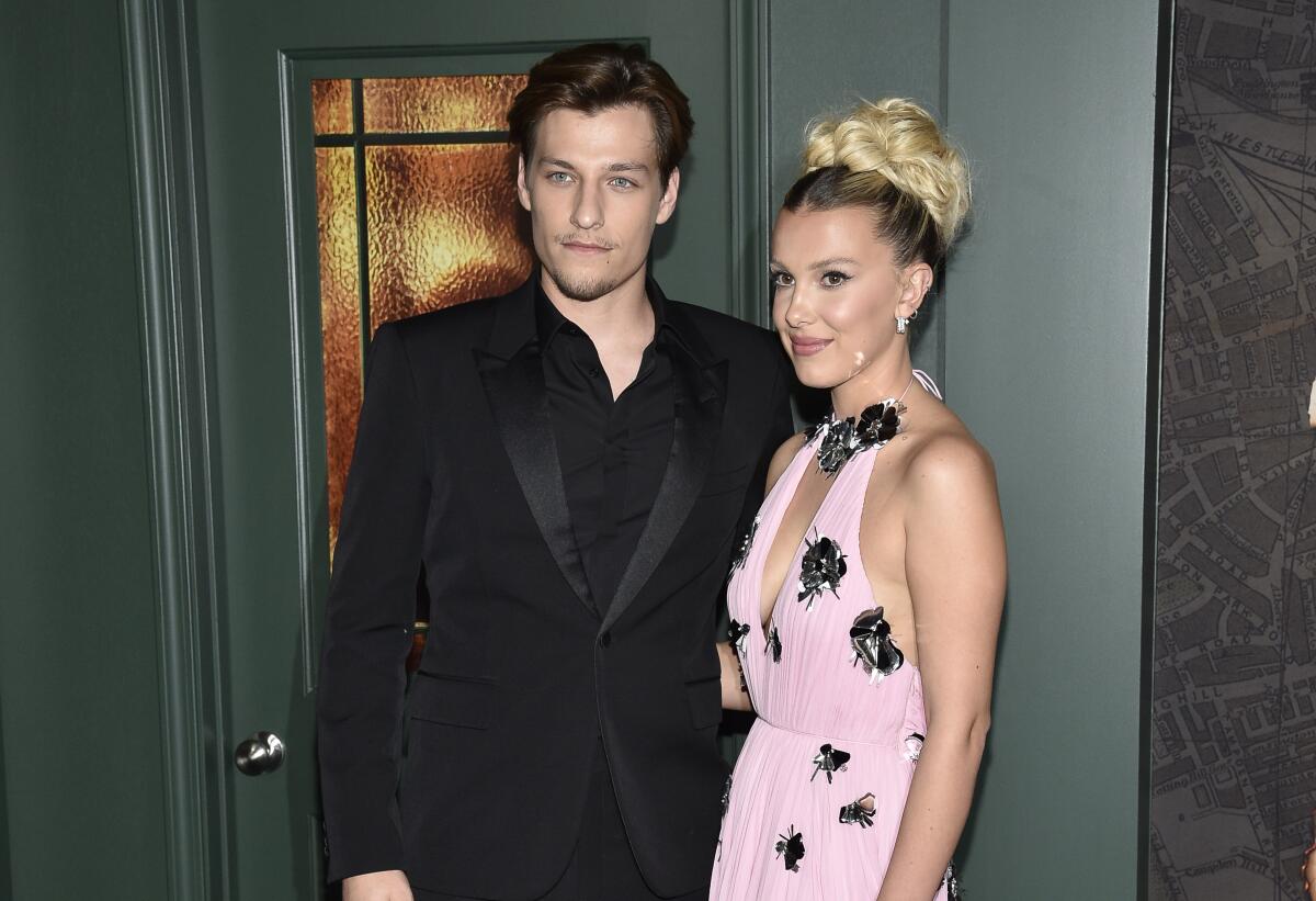 Millie Bobby Brown stands in a pink-and-black dress close to Jake Bongiovi, in a black tux and shirt with no tie