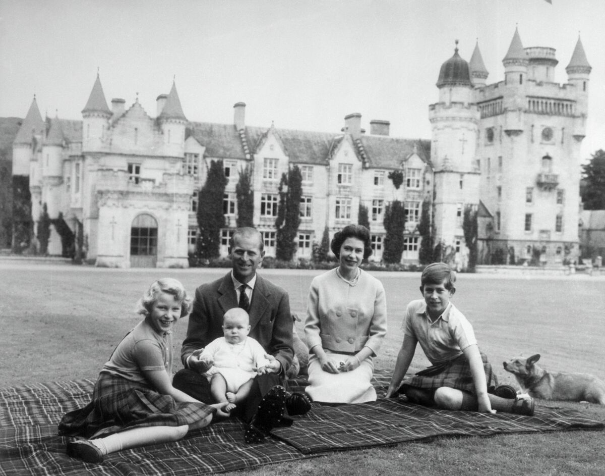 A royal family sitting on a picnic rug outside a large castle.
