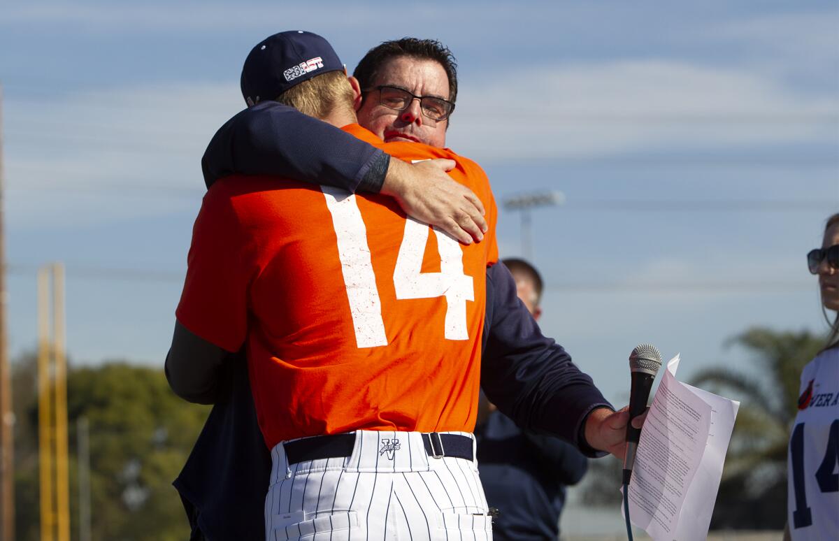 Tony Altobelli, Orange Coast College's sports information director, right, and acting head coach Nate Johnson, left, share a hug during a tribute for John Altobelli before Tuesday's game against Southwestern.