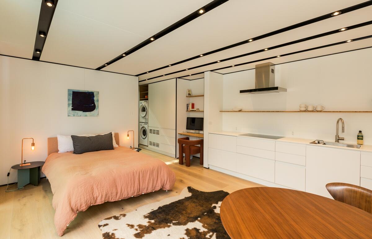 A small, white kitchen on one wall of an ADU, with a bed and a dining table nearby.