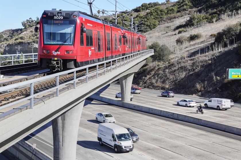 The San Diego trolley rides along the tracks as cars move along Interstate 8.