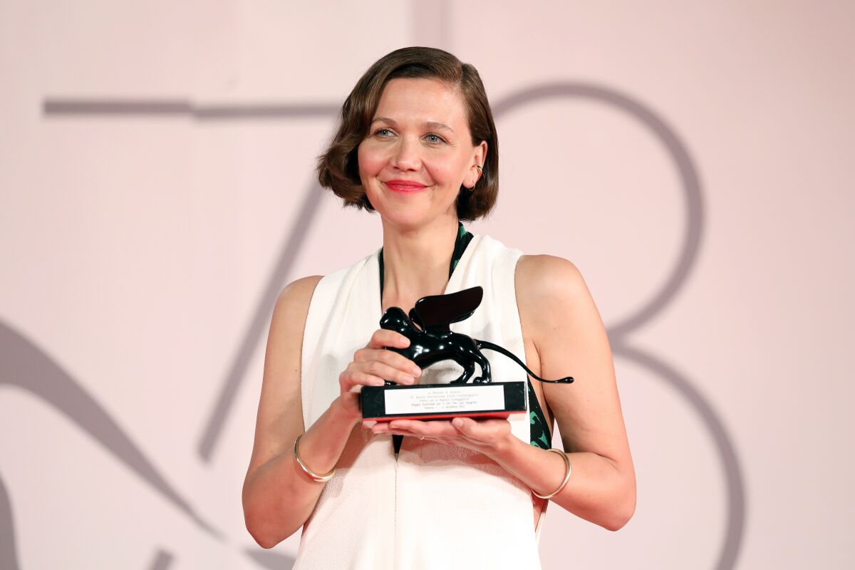 A woman with short hair holds up a statuette 