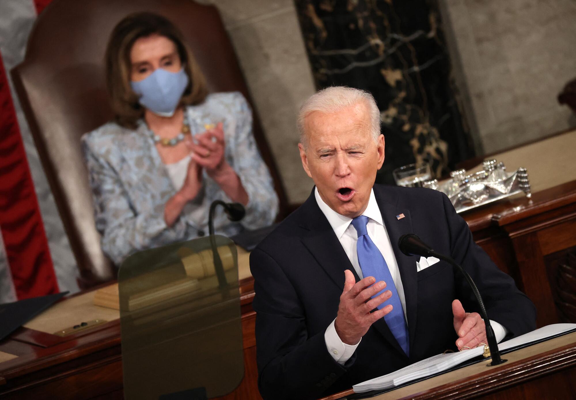 President Biden speaks as Nancy Pelosi sits behind him.