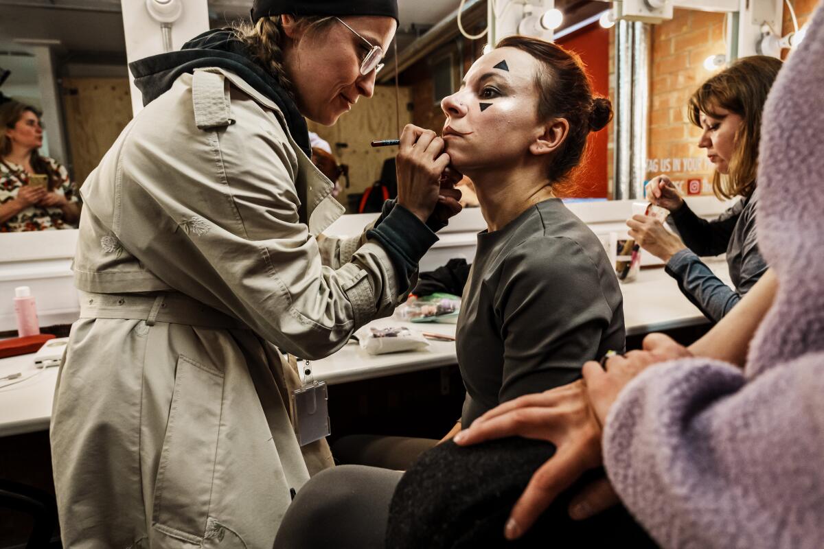 A woman puts makeup on an actor playing the Fool in "King Lear." 
