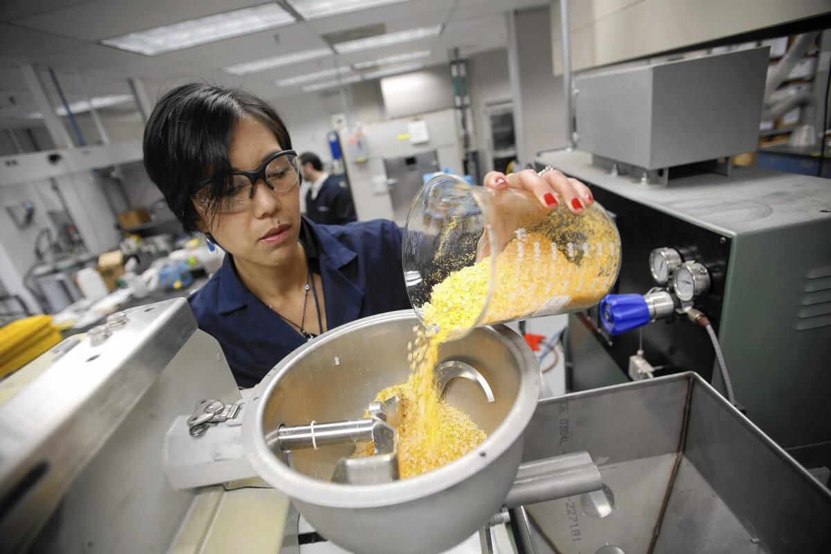 Ellen C. Lee pours a mixture of tomato fiber and polypropylene into the hopper of an extruder at a Ford lab. The company is looking into turning tomato skins into floor mats.