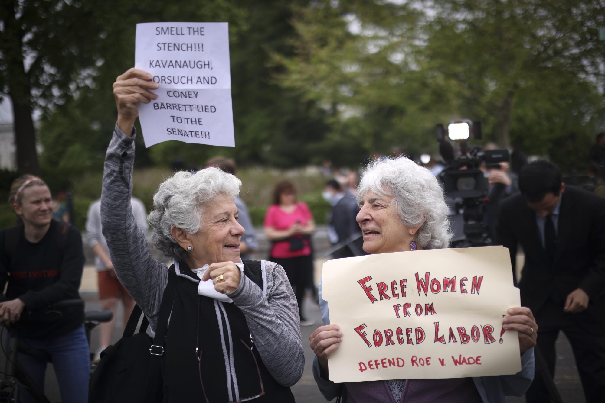 Two silver-haired women hold signs. One reads, "Free women from forced labor." 