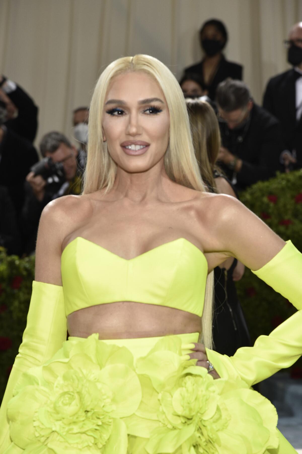 A blond woman poses with her hand on her hip while wearing a bright yellow two-piece gown with gloves