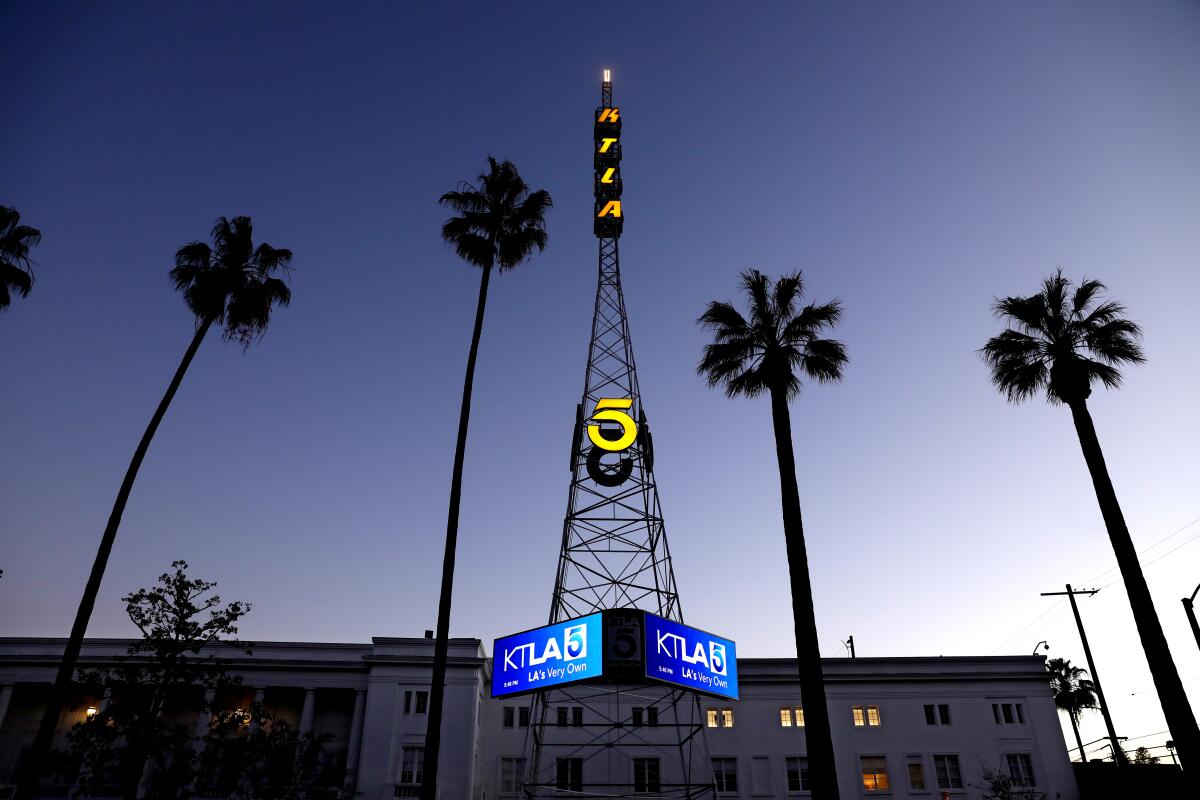 A TV transmission tower flanked on both sides by palm trees rises in front of a low building
