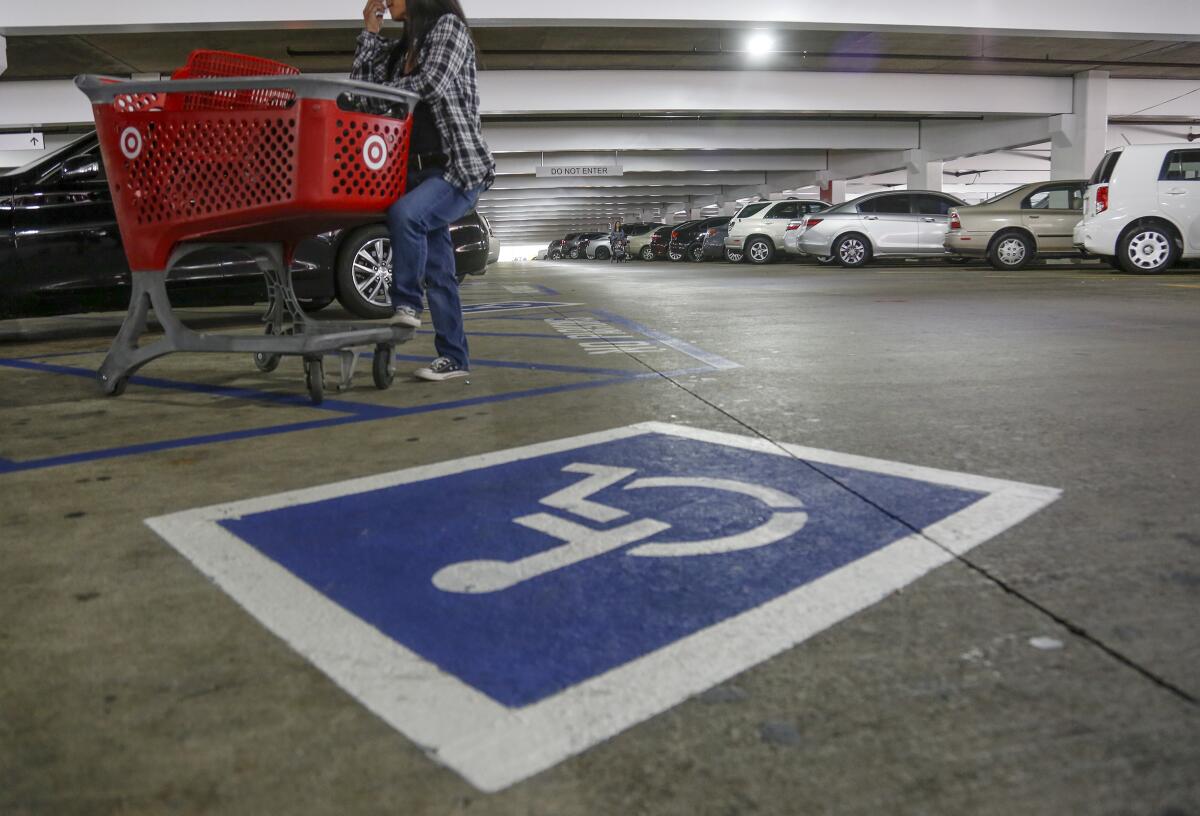 A low-angle frame of a parking garage. A person with a shopping cart is standing next to a disabled parking spot 